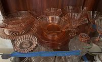 Full lot including various pink Depression glass dishes, plates, candy dishes, goblets, and candlesticks displayed in a cabinet.