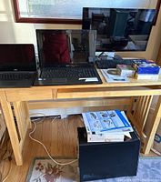 Wide view of table showing two laptops (Acer and Dell), Dell LCD monitor, keyboard, boxed floppy disks, and external hard drive in black case under table.