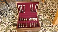 Full view of Oneida silver tone flatware set for 8 with serving pieces in wooden hard case with burgundy fabric lining.