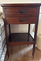 Front view of the side table showing two drawers with wooden round knobs and the lower shelf and legs.