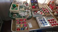 Display of multiple vintage Christmas ornaments arranged on table including boxed ornaments and figurines