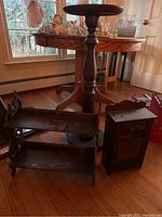 Three vintage shelves grouped on the floor: a tall round wooden plant stand, a two-tiered wooden shelf turned sideways, and a small glass-fronted wall shelf missing its knob.