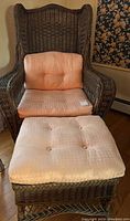 Wicker armchair with light peach cushion and matching ottoman in front of floral wallpaper.