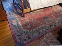 Floral area rug with red and blue borders, floral patterns, visible wear and damage visible near furniture on hardwood floor.