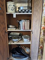 Photo showing various metal baking pans including cupcake pans, rectangular baking sheets, a stockpot, and strainers arranged on shelves