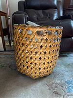 Front view of large round woven basket on carpet near leather chair showing open weave pattern and thickness of weave.