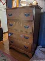 Front view of wooden chest of drawers showing four drawers with black metal handles and visible finish wear on bottom drawer.