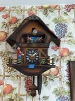 Front view of the cuckoo clock showing the chalet style wooden design with clock face and figurines.