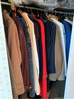 Photo shows a variety of medium to large sized women's and men's jackets, leather jackets, raincoats, sweaters, and blazers hanging on a rod.