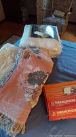 Overview of comforter in packaging, fringed blanket, and two Thermophore heat pack boxes