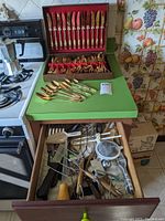 Full view of the goldtone stainless steel cutlery set boxed, plus the kitchen drawer with assorted utensils.