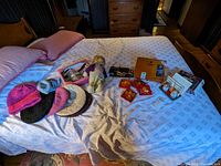 Overview of lot items on bed including crocheted hats, vintage doll, ceramic and plastic angels, sewing trims, box, metal car wheels