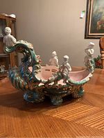 Front view of vintage ceramic boat planter with cherubs showing worn areas and intricate design