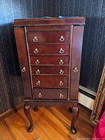Wood look jewelry armoire with six drawers, side doors closed, and standing on cabriole legs