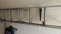 View from top showing rungs and side rails of 16ft aluminum extension ladder hung horizontally on garage wall brackets.