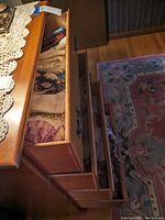 Wooden dresser with open drawers showing a variety of folded linens including scarves, doilies, and place mats.
