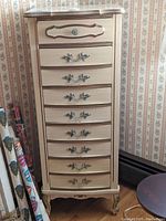 Front view of lingerie dresser showing 7 drawers with ornate metal handles, light wood finish, and French provincial styling.