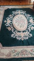 Full view of rectangular floral area rug with green field and cream border showing overall design and condition.
