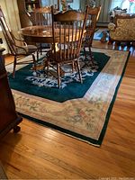 Rug in navy blue with ivory and pink floral border placed on hardwood floor under dining table with wooden chairs.