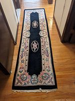 Full view of the black floral runner rug with a central black field and pastel floral border on wooden floor.