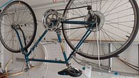 Side view of blue Schwinn Varsity bike hanging from ceiling showing frame, tires, pedals, chain, and part of handlebars.