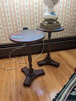 Two matching wood look round side tables with turned pedestal bases and visible scratches.