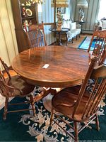Round pedestal dining table with leaf and four spindle back chairs around it on floral carpet in a room with vintage decor.