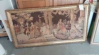 Full view of large rectangular tapestry with dance scene in ornate wood frame showing detailed figures in period costume and outdoor terrace setting.