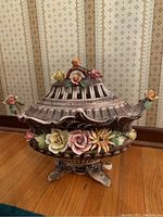 Front angle view of ornate tureen showing detailed floral decoration, lid with lattice work and pedestal base.