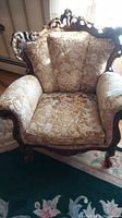 Full view of vintage floral upholstered armchair with carved wood frame and padded arms on a rug.