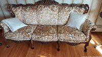 Full view of vintage sofa showing carved wood frame and floral upholstery with three cushions and two pillows