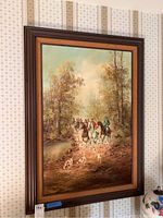 Full view of the oil painting showing horse riders with dogs in a wooded landscape with river, framed in dark brown wood and burlap frame.