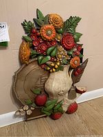 Front angle view of the colorful resin wall sculpture featuring flowers, leaves, vase, and fruit with a beige textured vase and bold floral colors.