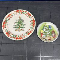 Both Christmas-themed plates arranged side by side on a black grid surface, showing the detailed decoration of both items.
