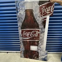 Full front view of the large vertical metal Coca-Cola vending machine sign showing a detailed image of a Coke bottle with ice and condensation and the Coca-Cola logo at the top.