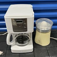 Mr. Coffee white coffee maker with glass carafe and digital panel shown alongside Oster Imperial juicer with clear plastic lid.