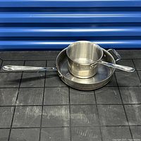 Photo showing the 3 Quart saucepan with lid placed on the 2 Quart sauté pan, both stainless steel with copper core, on black surface with blue backdrop.
