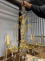 Full view of gold-toned metal chandelier with hanging crystal strands and eight candle-style bulb holders, displayed in storage.