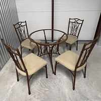 Photo of dining table and four matching chairs from front angle showing metal frame detail and beige cushioned seats.