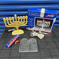 Yellow electric menorah with power cord, box, bulbs, and Ten Commandments glass tablets on black surface.