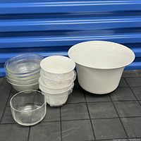 Mixed serving bowls displayed against a blue background on a gray grid surface, showing a stack of four textured clear glass bowls, a single 7-inch clear glass Pyrex bowl, and two white plastic bowls (one large, one small).