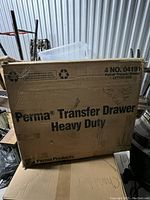 Large cardboard box featuring printed text 'Perma Transfer Drawer Heavy Duty' and recycling logos. Box is worn and marked with handwriting.