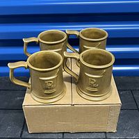 Four brown ceramic mugs arranged on a cardboard box showing the embossed Rx symbol on two mugs
