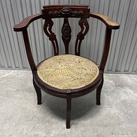 Front view of wooden accent chair with carved backrest and round upholstered seat showing wear and staining.