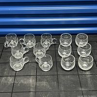 Front view of 14 small clear glasses and mugs arranged in rows, 7 with handles and 7 without handles