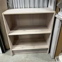 Front view of small white wood bookcase with two shelves and visible wood grain finish.