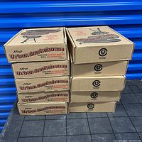 Ten stacked Urban Smokehouse cardboard boxes on a black floor with blue background, showing branding and product name.