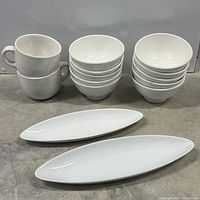 Top view of six cups stacked beside six small bowls and six larger bowls with two elongated platters in front.