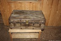 Front view of antique leather trunk showing metal clasps and lock mechanism, leather straps and corner protectors.
