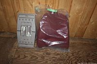 Photo showing the maroon ObusForm backrest cushion wrapped in plastic next to the gray folding step stool against a wood backdrop.